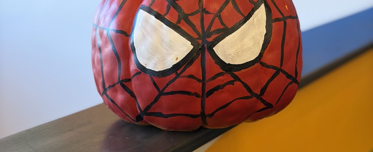 Pumpkin painted like Spider-Man’s mask, sitting on a ledge in front of a colorful clinic mural.