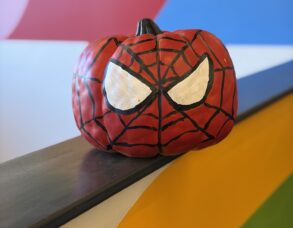Pumpkin painted like Spider-Man’s mask, sitting on a ledge in front of a colorful clinic mural.